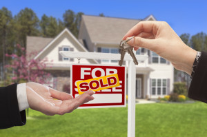 Real Estate Agent Handing Over the House Keys in Front of a Beautiful New Home.